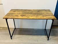 Front view of desk showing wood effect MDF surface and black steel legs on laminate floor