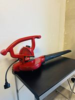 Full view of the red Toro corded leaf blower on a black table against a white wall, showing the handle, body, and air nozzle.