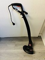 Full view of the black electric corded weed eater with ergonomic handle and power cord.