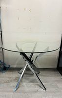 Front view of a round glass dining table with chrome intersecting legs.