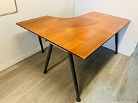 Front view of the L-shaped desk showing natural wood surface and black legs