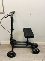 Side angled view of black knee scooter with padded knee rest, showing frame, wheels, and handlebar with brake lever
