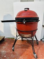 Full front view of the red ceramic grill on its cart with side shelf extended