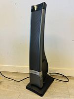 Front view of black and silver Lasko tower heater standing on a wooden floor.