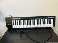 Full view of the M-Audio Keystation 49es MIDI keyboard controller showing all 49 keys and USB cable on black surface.