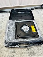 Top view of the portable gas stove and carrying case with the stove wrapped in plastic and placed inside the hard black case.