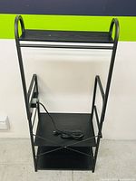 Side/front angle view showing three black shelves on black metal frame, highlighting size and shape of shelves including curved side handles on top shelf.