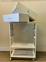 Side view of the white storage cart showing an open drawer and the wrapping paper holder attachment.