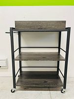 Front view of the rolling cart showing three wooden shelves and metal frame with caster wheels