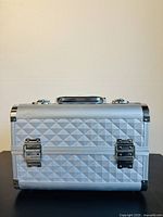 Front side of silver diamond patterned makeup train case showing two silver metal latches and textured outer surface.