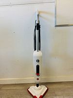 Full view of the white Hoover steam mop with a triangular mop head with red trim and black cord.