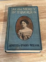Blue cloth hardcover antique book with gold embossed title and author's name, featuring an oval portrait of a woman on the front cover.