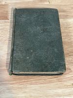 Closed antique book with dark, worn cover showing some embossed floral patterns, edges worn, spine intact