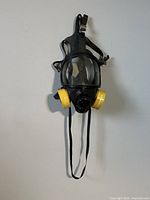 Front view of black full face respirator mask with yellow cartridge filters attached on each side and adjustable straps.