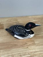 Side profile view showing detailed coloring and shape of the loon coin bank resembling a bird with red eyes and white dots.