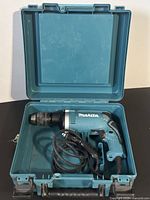 Makita hammer drill inside blue hard plastic carrying case with cord coiled next to it