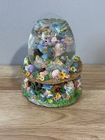 Front view of the musical snow globe showing bunnies inside and colorful flower and ladybug decorated base.