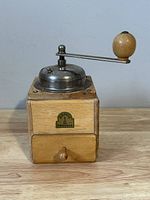 Front view of the vintage Armin Trosser coffee grinder showing wooden body, metal grinder top, crank handle with wooden knob, and brand plaque.