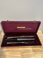 Opened maroon box with carving knife, carving fork, and sharpening steel inside, visible Community Plate label.