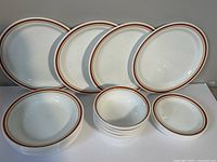 Photo showing 10-inch dinner plates, 9-inch plates, bowls, and saucers with brown and orange double rim design arranged on a table.