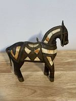 Front-side view of carved wood horse sculpture showing inlaid stone or bone pieces with geometric patterns and brass chain detail on head.