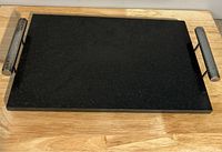 Top view of rectangular black marble tray with metal handles on short sides, placed on wooden surface.