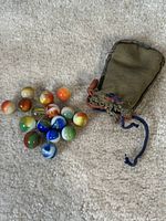 16 vintage glass marbles in various colors arranged near a vintage drawstring pouch.