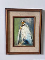 Full view of framed vintage oil painting depicting a figure in white coat and hat with small animal
