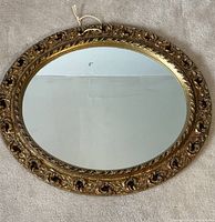 Top view of the vintage oval wall mirror laying flat, showing gold tone decorative carved wood frame and clear glass reflective surface.