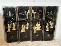 Four vertical black lacquer wall panels with detailed mother of pearl inlay depicting Asian geisha women, scenic backgrounds, and bordered patterns, photographed against a white wall.