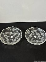 Two matching clear glass bowls with scalloped edges and embossed floral design, placed side by side on a black surface