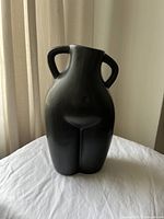 Image of the front side of the ceramic black vase shaped as a human lower torso with two handles.