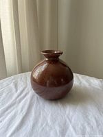 Front view of the small round ceramic burnt red vase on a white surface with curtain background.