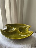 Side angled view of a green ceramic serving platter divided into three compartments with a central hole.