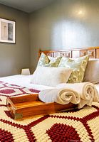 Side view of a bed showing the wooden headboard with carved square panel detailing, pillows, and bedding in a neutral bedroom setting.