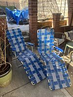 Pair of vintage lawn chairs with blue woven vinyl strapped seats and backs, metal frames, and footrests, shown outdoors on a patio.