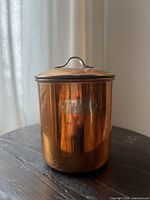 Front view of the vintage copper canister showing the metallic 'Cafe' label and lid handle.