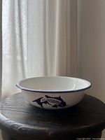 Side profile of the medium white enamel bowl showing blue fish motif and blue rim on a wooden surface.