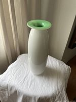 Photo of the full white vase with green rim placed on a white cloth against a curtain background.