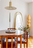 Living room setting with large vertically standing gold orbit mirror leaning against the wall, next to a tall orange floor lamp and houseplant.
