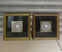 Two small framed sun face prints side by side showing black and white radiating rays and gold background