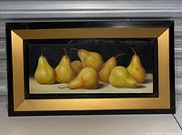 Front view of the framed painting showing nine yellow pears on a dark background within a black and gold frame.