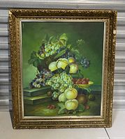 Full frontal view of vintage fruit still life painting on canvas showing grapes, pears, apples, melon on a dark green background inside an ornate gold frame.