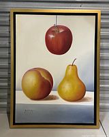 Full view of the framed vintage still life painting showing a hanging red apple, a peach, and a yellow pear on a neutral background with the artist's signature.