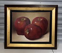 Full view of the painting with three red apples in a wooden frame with gold trim