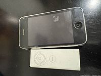 Apple iPhone 3GS laying beside white Apple TV remote control A1156 showing circular navigation buttons and menu button.