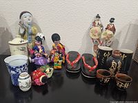 Wide view of various Asian decor and ceramics items including figurines, dolls, pottery, and wooden sandals arranged on a shelf.