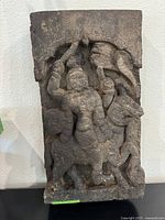 Full view of the burnt hand-carved wooden sculpture depicting Hindu deity riding a horse, showing charred surface and overall shape.