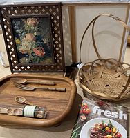 Photo of two wooden charcuterie platters, wooden utensils, wicker tray, wicker basket, Better Homes and Gardens Fresh cookbook, and floral print in wicker frame arranged together.