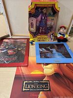 Disney collectibles lot showing Mulan doll in box, Lion King special edition lithograph set, Alice in Wonderland Tweedle Beanie, Chip 'N Dale figure, a small male character figure, and blue Smurf figure.